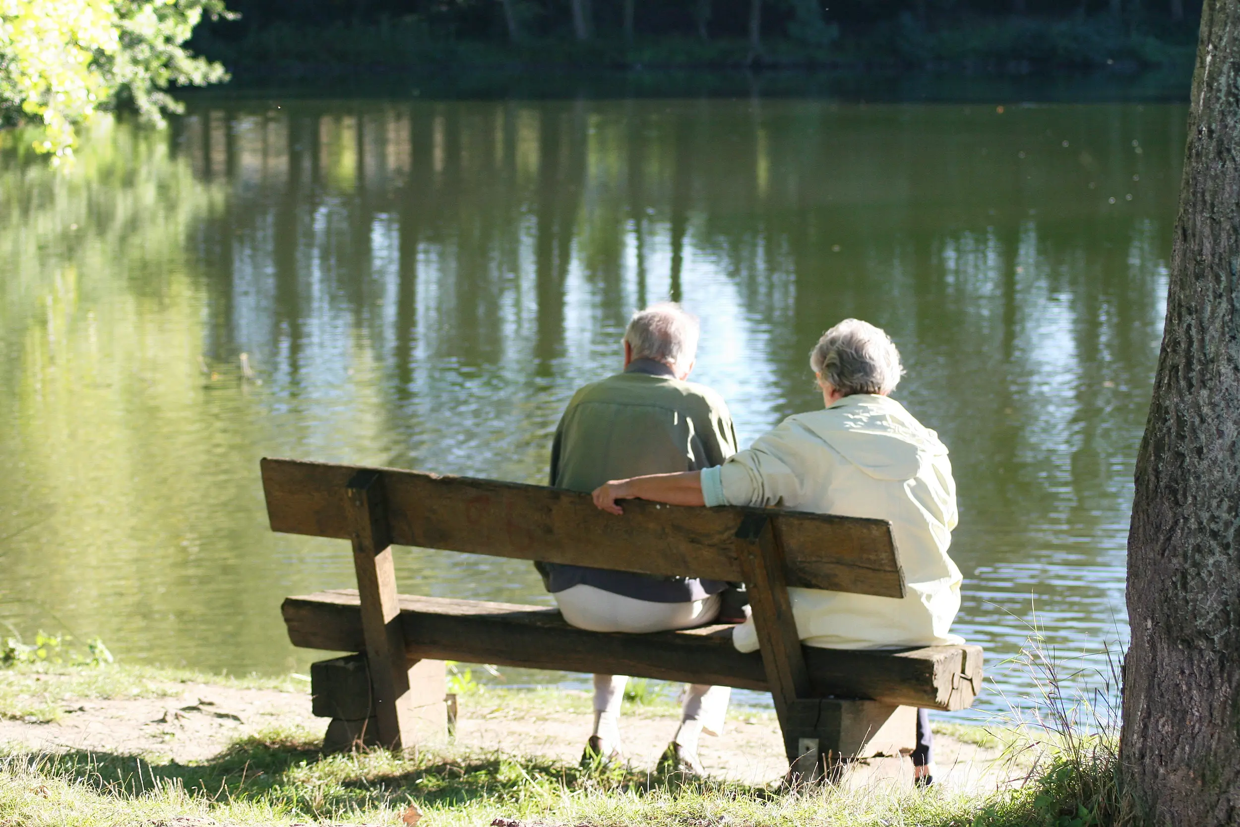 Pareja mayor sentados en una banca a la orilla de un lago