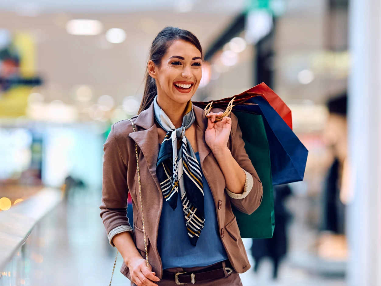 Mujer caminando en un centro comercial con bolsas de compras, representando beneficios y recompensas por ser cliente BCR.