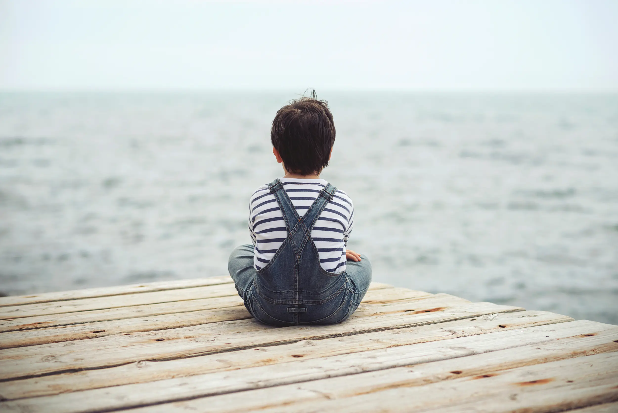 Niño sentado en un muelle viendo al horizonte